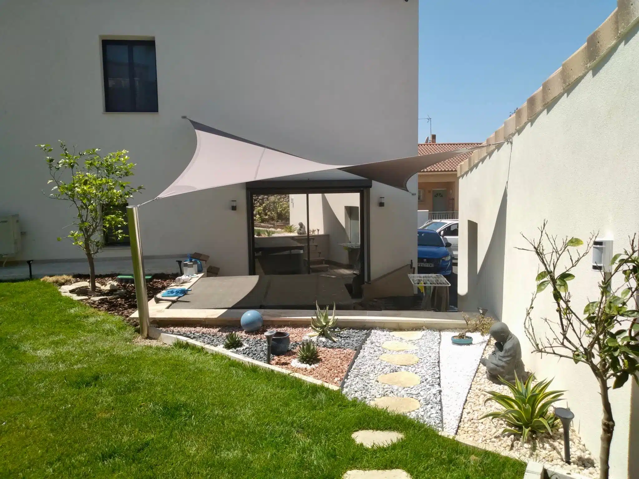 Espace extérieur aménagé avec une voile d'Ombrage sur-mesure, fixée à un poteau en INOX
